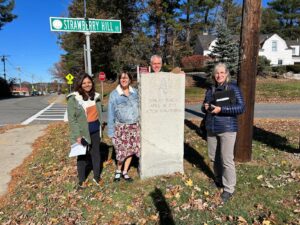 A group of people around a stone marker and street sign
