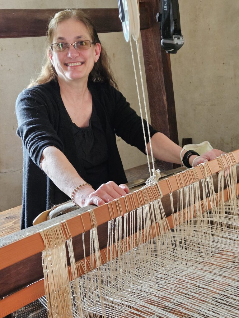 A woman stands behind a loom