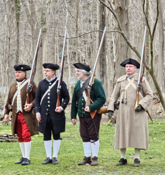 four men in Revolutionary clothing stand holding long-barreled firearms