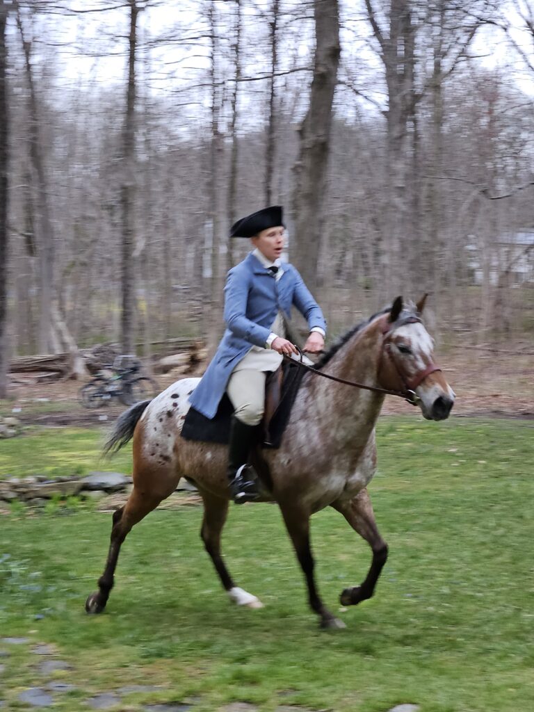 Man in a blue revolutionary era coat and tricorner hat riding a horse.