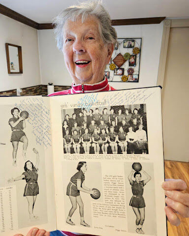 Woman with gray hair proudly shows off the basketball page from her high school yearbook (circa 1955).