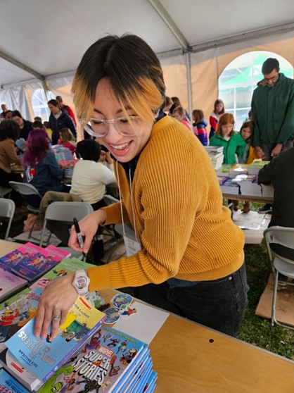 Woman with orange and brown hair smiles as she takes a book to autograph.