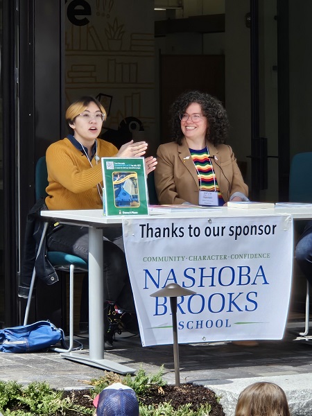 Two women sitting at a table. The one on the left is speaking animatedly.