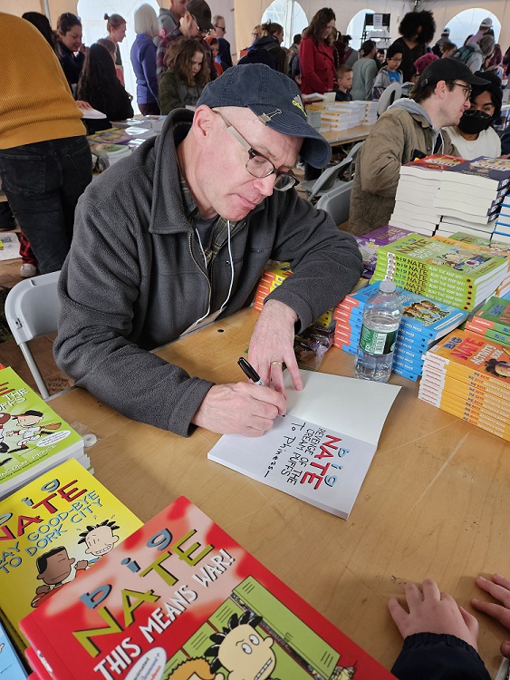 Man with baseball cap signing one of his books.