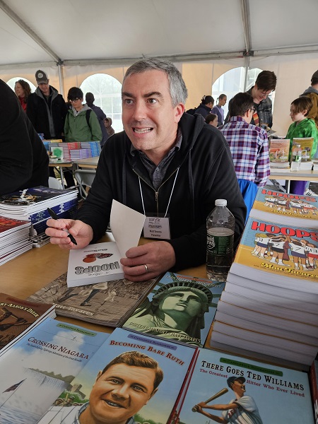 Gray-haired man with a pen and a book also have a conversation with whoever is waiting for his autograph.