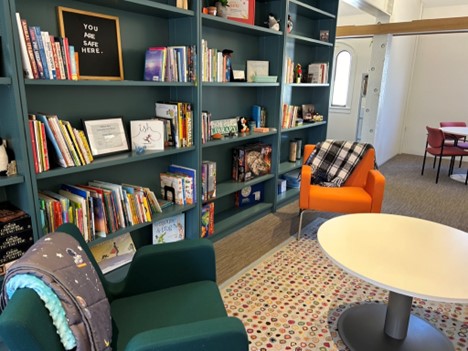 A room with comfortable chairs, a colorful rug, shelves full of books and a sign that says "You are safe here."