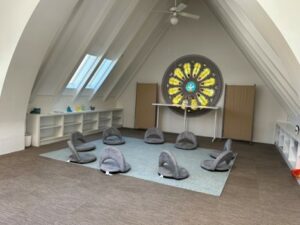 An alcove inside Danny's Place with a rose window and low grey cushions with backs in a circle on the floor.