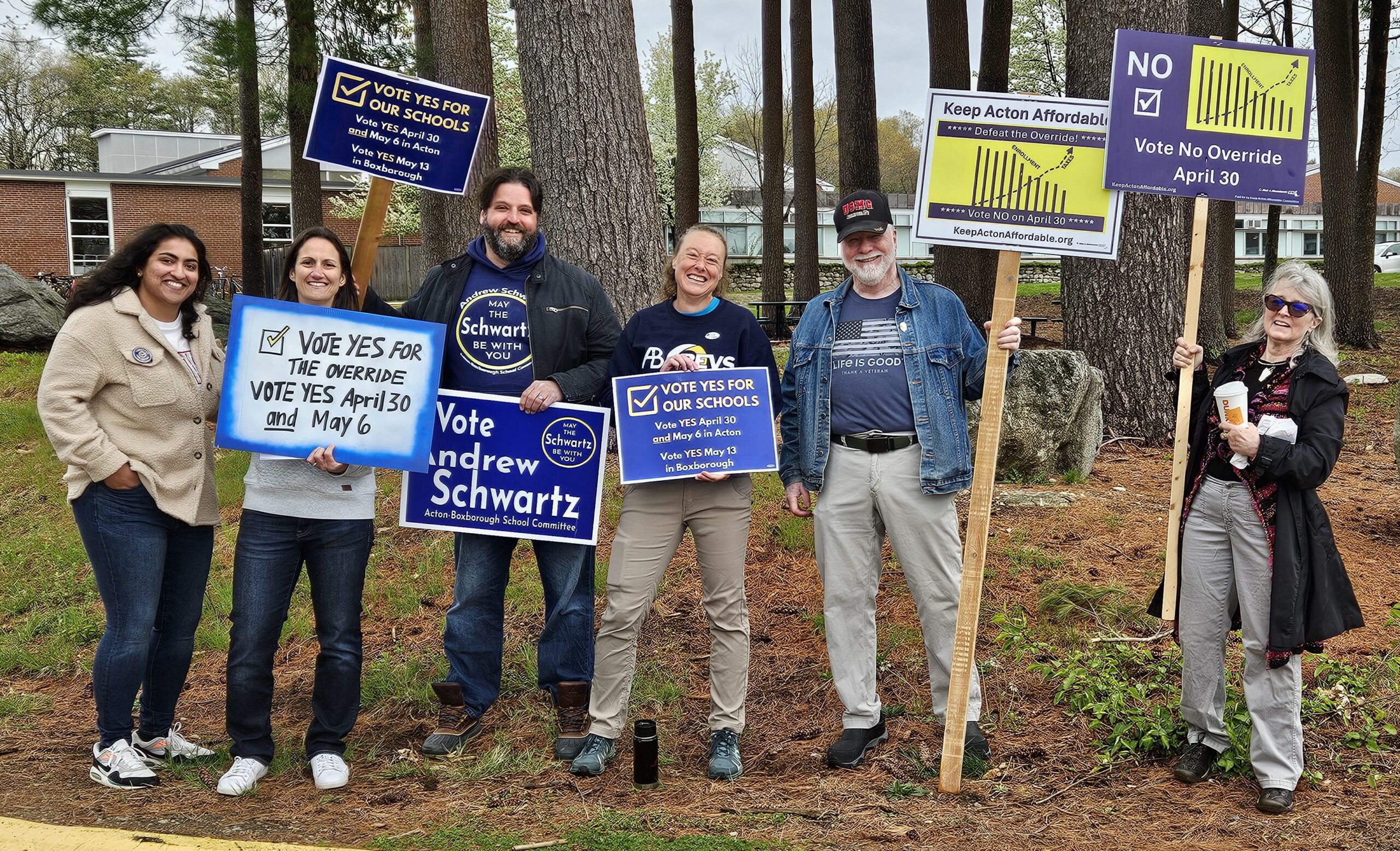 A group of 5 people smiling and holding political signs both for and against the override, Andrew Schwartz is also there, holding an Andrew Schwartz for School Committee sign.