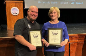 A man and a woman holding award plaques at Town Meeting.