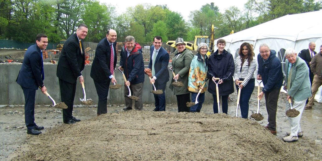 A large group of people pose with shovels full of dirt.