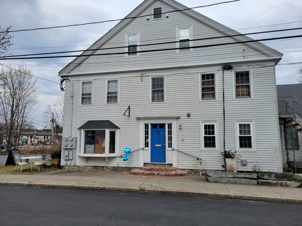A white older building with a bright blue door and brickwork stairs.