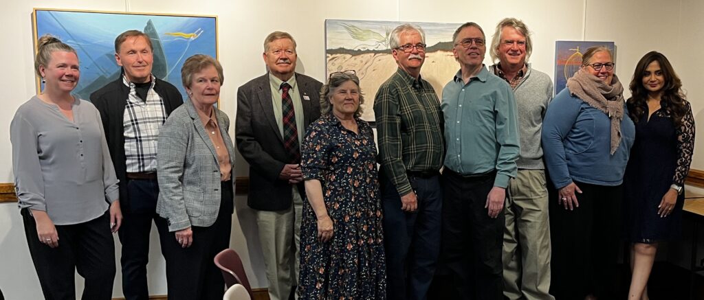 A group of people stand in front of the art in the Acton Memorial Library meeting room.
