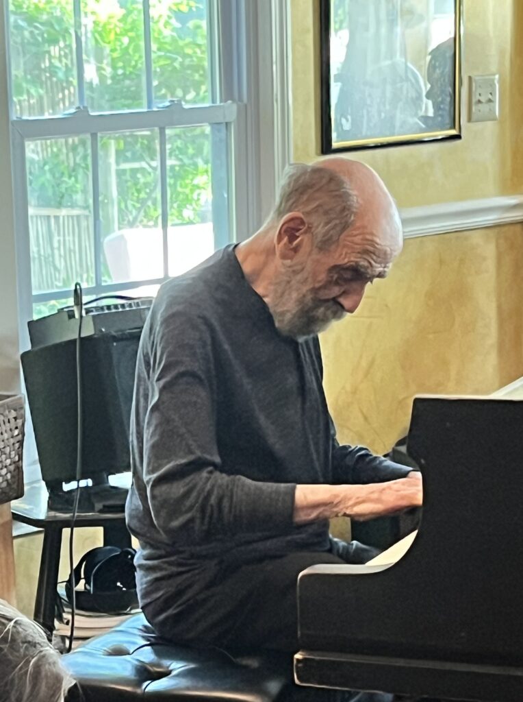 An older man concentrating on the piano keys. He's casually dressed in a grey sweatshirt.