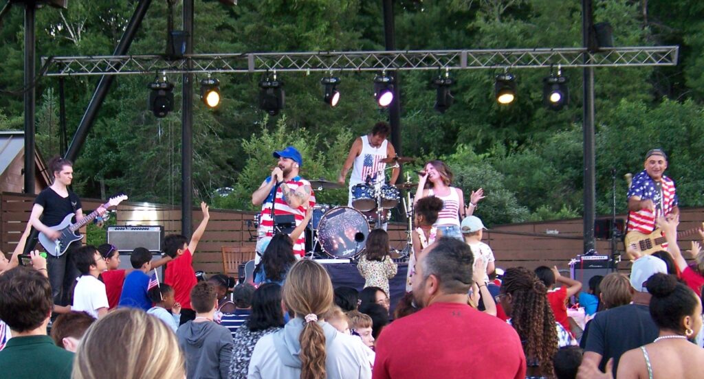 Four members of a band at the NARA park bandshell are clad in red, white, and blue. The base player didn't get the memo and is wearing a black t-shirt.