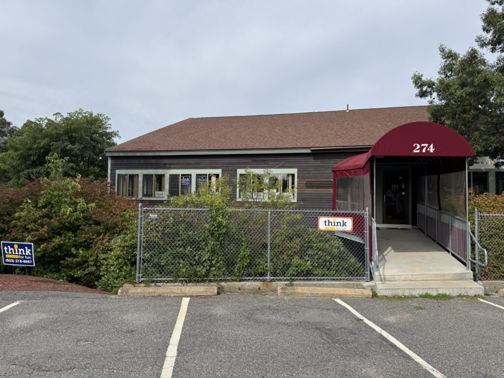 A brown building with a long maroon awning over the entranceway. A small sign on the fence says "think" in lower case letters.