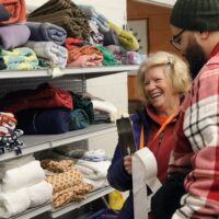 A smiling older woman helps a younger man who is only seen in profile.