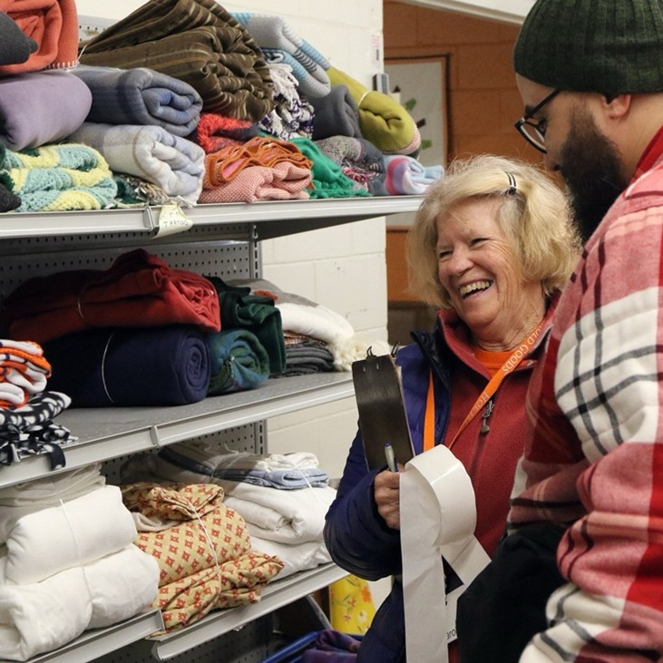 A smiling older woman helps a younger man who is only seen in profile.