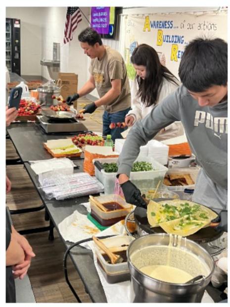 Three people serving food. The person in the front is making a thin pancake.
