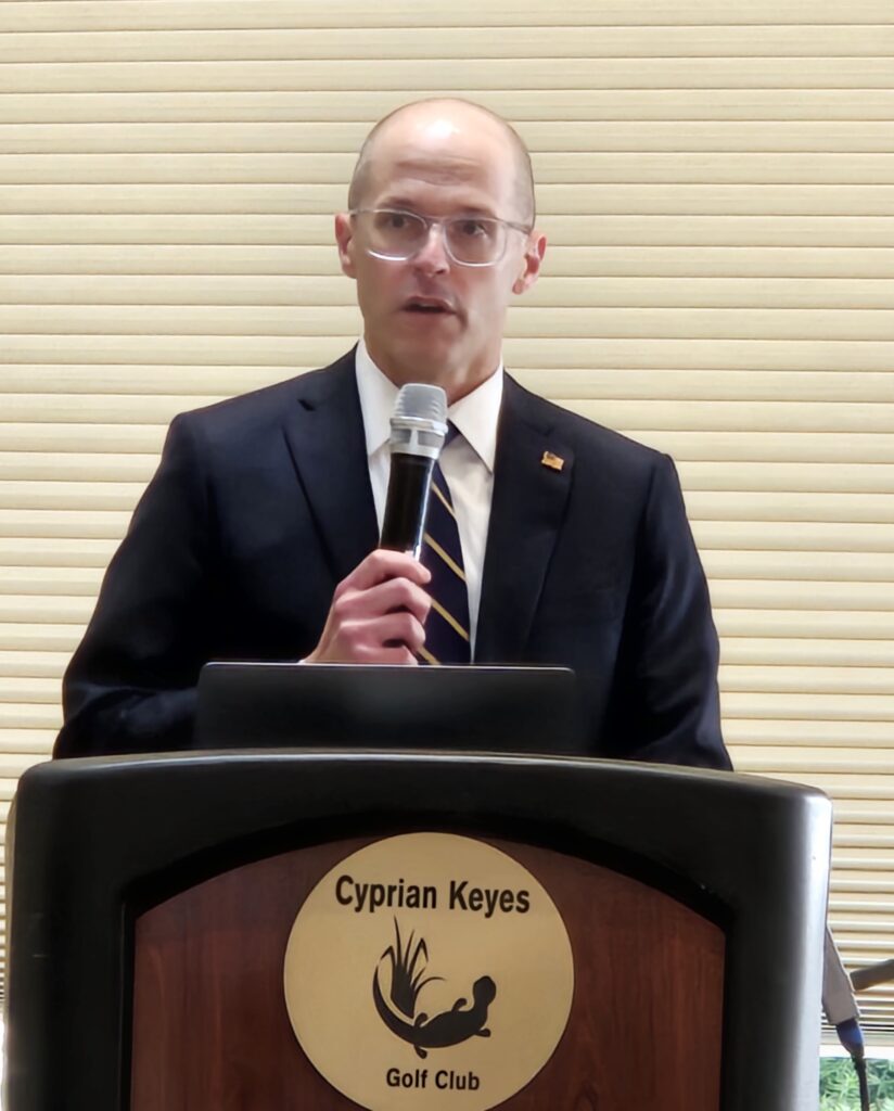 A balding man with glasses speaks at a podium.
