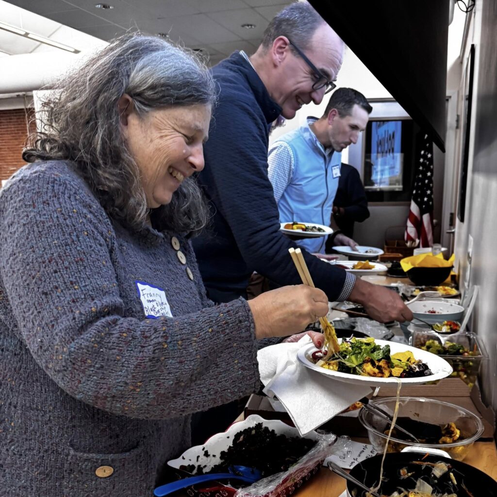 Three people are lined up in front of platters of food, serving themselves. They seem to be enjoying themselves.