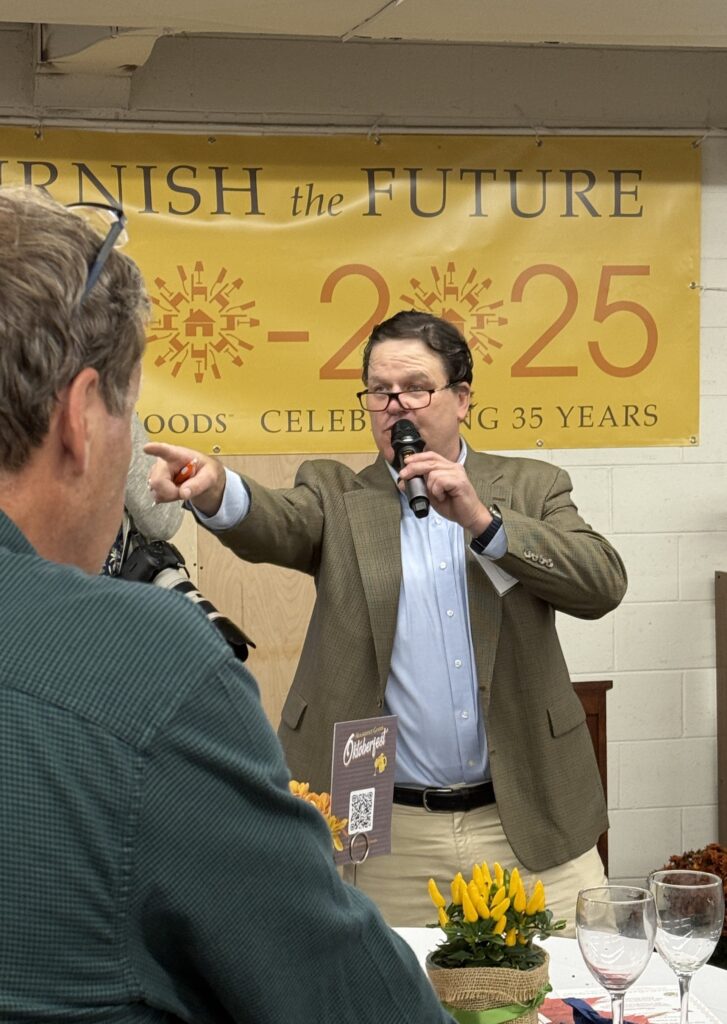 A man with a mic and glasses perched on his nose points at a member of the audience.