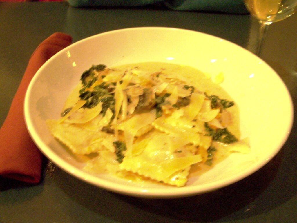 A large white bowl full of ravioli and broth.