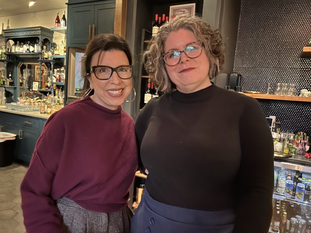 Two women stand in front of a restaurant bar.