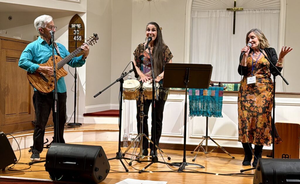 A man on the left plays a beautiful guitar. In the middle, a woman plays bongos, and on the left, another woman sings.
