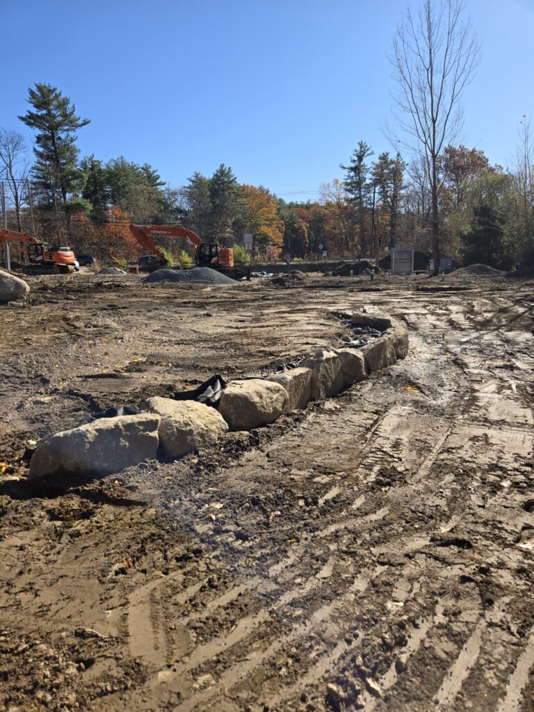 An arc of large stones stretches around a dirt field. There are excavators and piles of dirt in the background.