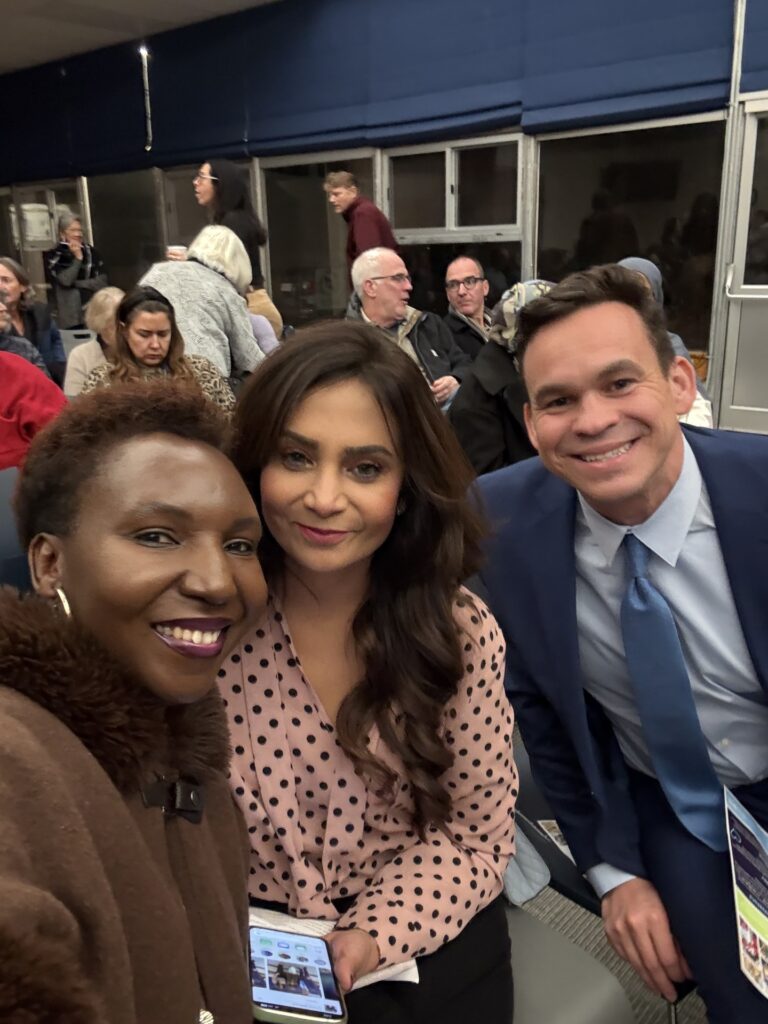 Three people sitting in a crowded room, smiling for the camera.