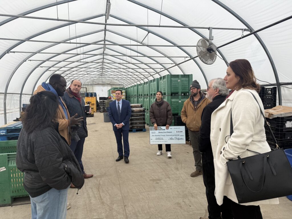 People standing in a greenhouse while a tall Black man speaks to them.
