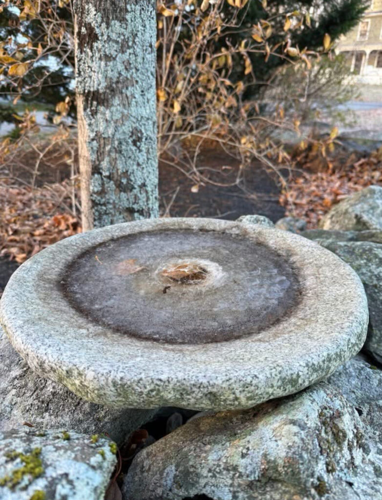 A perfectly round stone, wich a frozen puddle in the middle, rests on top of some natural stones.