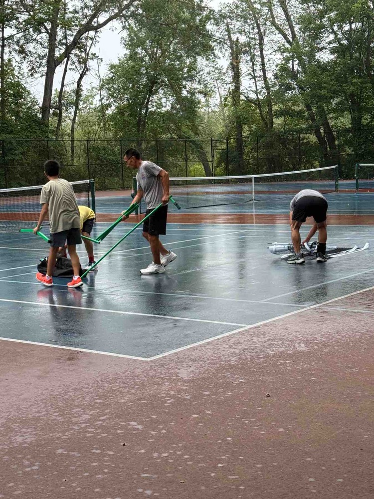 A handful of kids set up nets on a rainy court.