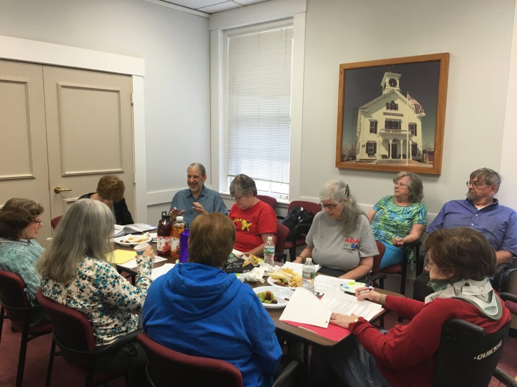 A group of people crowd around a table in Town Hall. There are notes and plates of food scattered on the table.