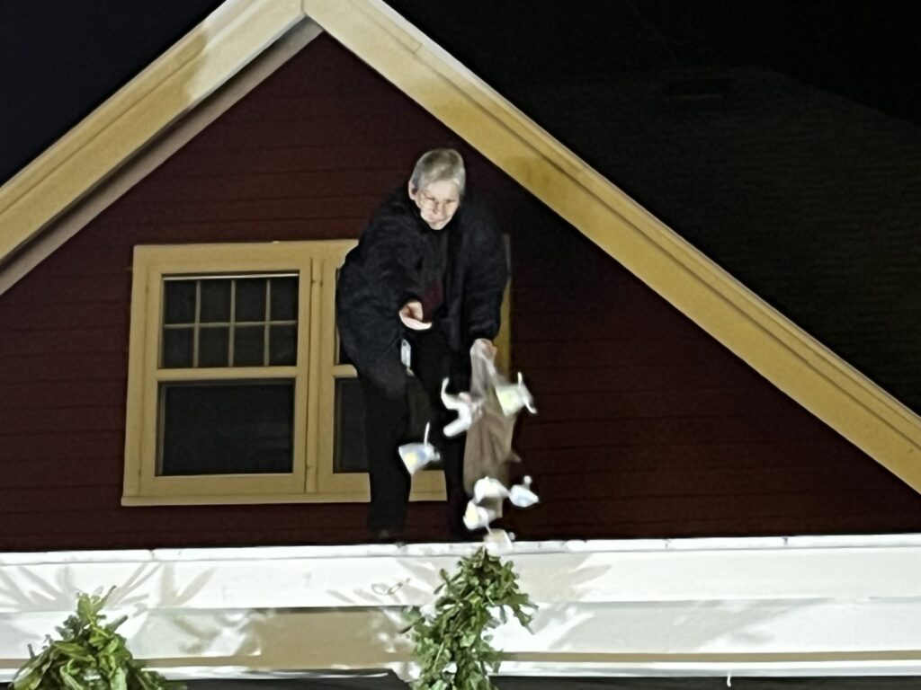 A woman in black tosses little bags down from the roof of the Red House.