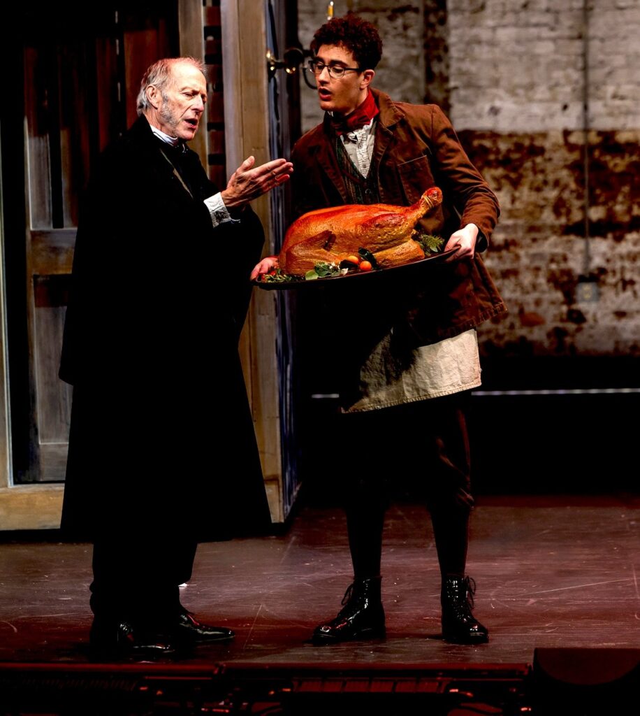 Two men in Victorian dress discuss a roast turkey that is being held by the younger man.