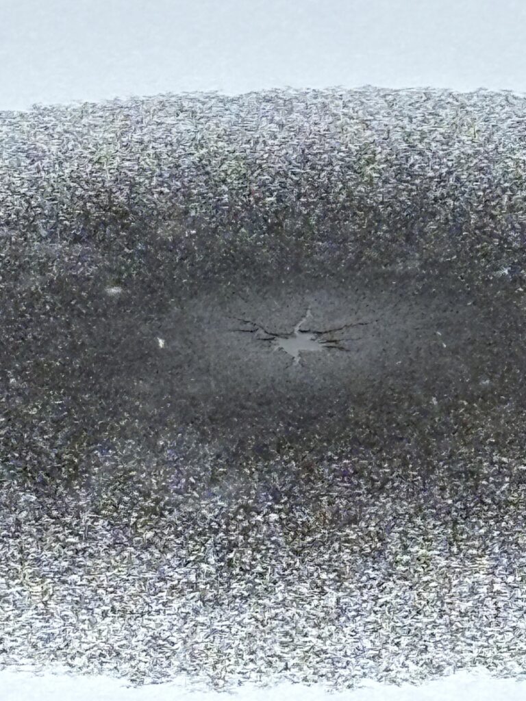 A small star shaped hole appears in the ice surrounded by a dusting of snow.