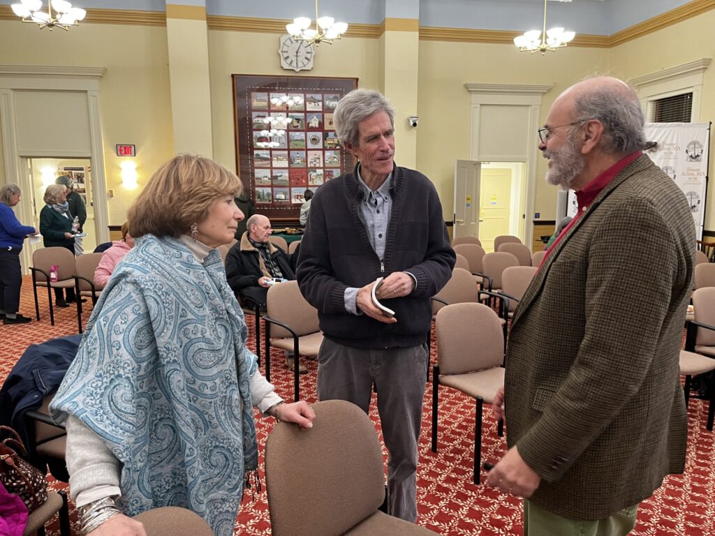 A woman and two men stand chatting in Room 204 of Town Hall.