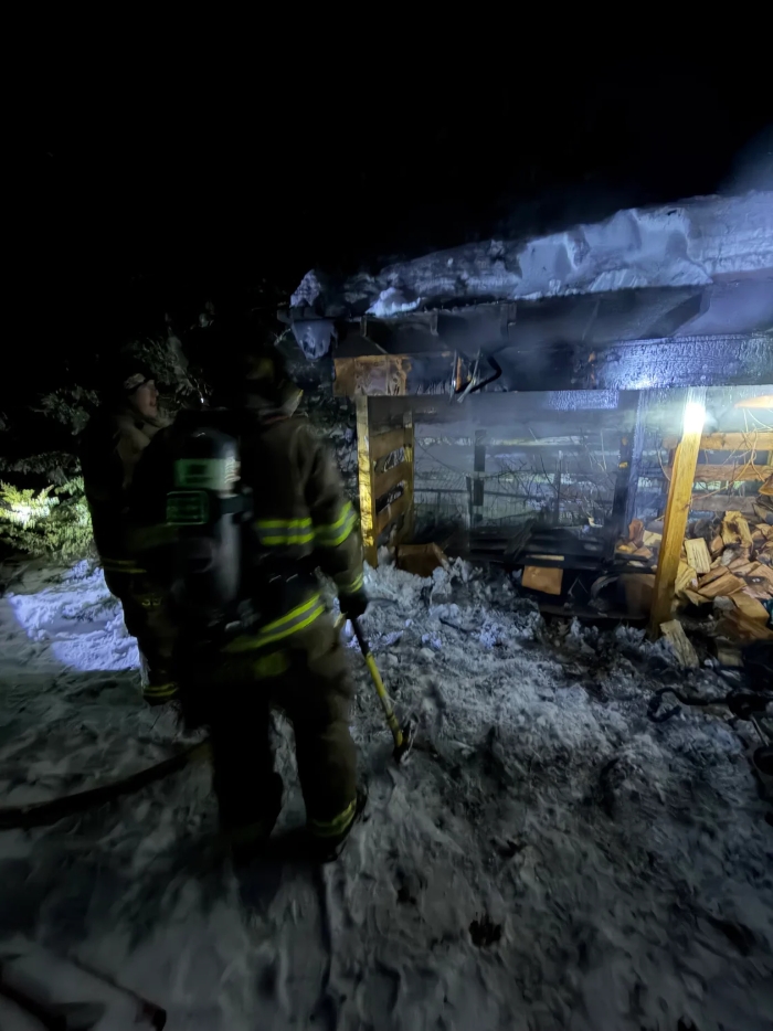 A firefighter holds an ax and shines a strong light into the remains of the shed to make sure the fire is completely out.