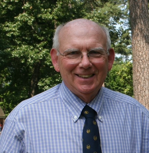 A smiling, balding man wearing wire-frame glasses and a blue shirt and tie.
