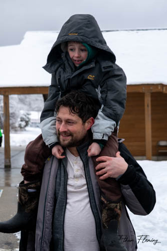 A small boy in a big parka sits on his dad's shoulders.