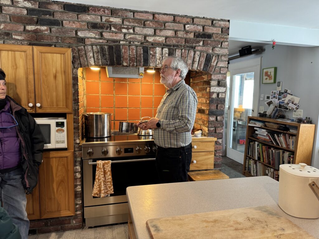 An older bearded man stands in front of an induction stove while holding a pot.