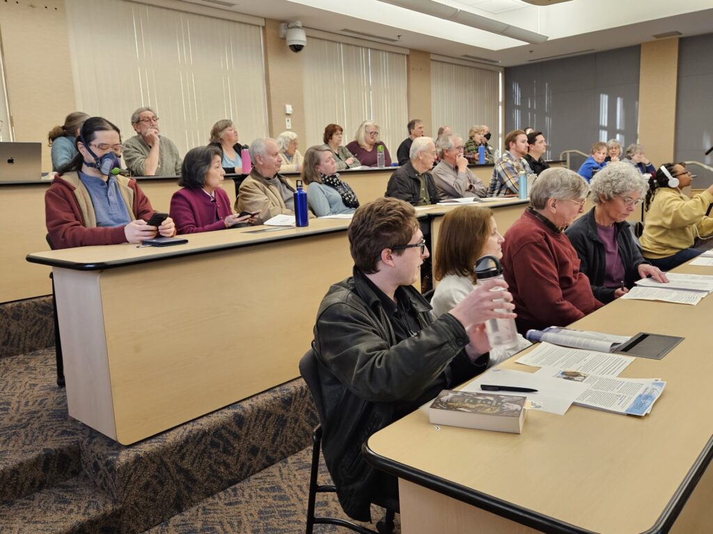 A room that is set up as a series of desks on risers with a person in just about every seat.