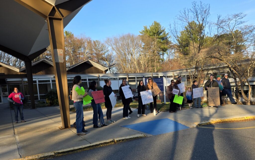 A group of people stand outside a building with signs that say " Equal Disruption is NOT Equity," and "Vote for Change".