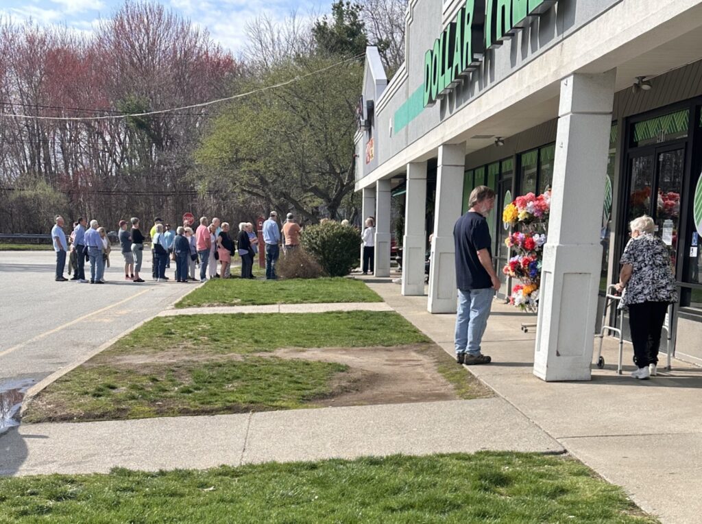 People standing in a line out the door and into the parking lot in front of a building.