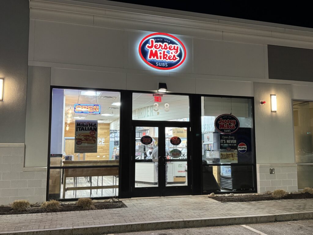 A Jersey Mike's storefront with a red and blue sign and white interior.