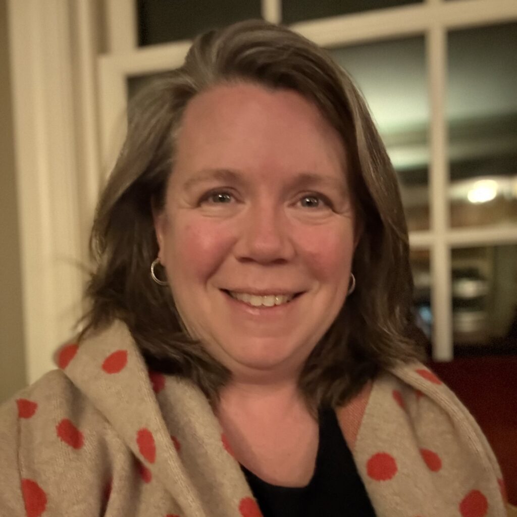 A smiling woman with chin-length hair wearing a seater with orange polka-dots.