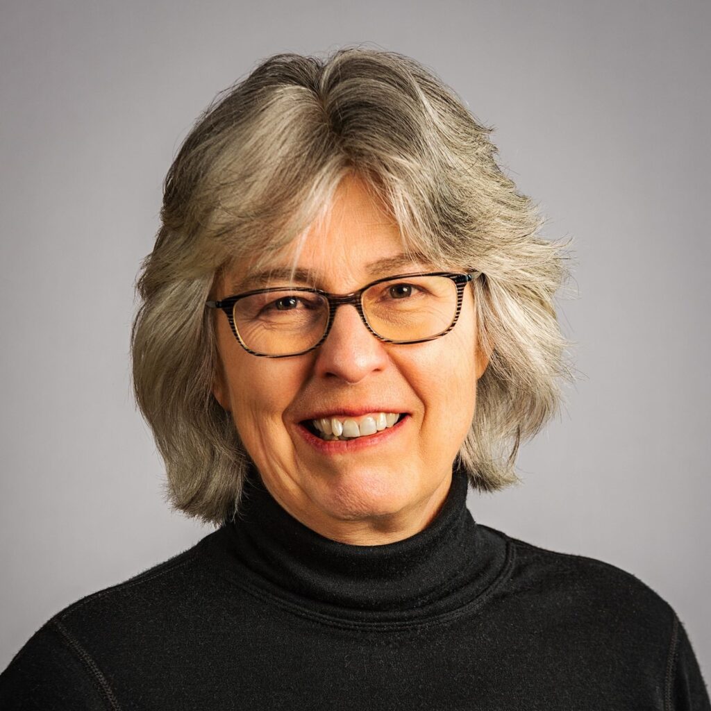 A smiling woman with short grey hair and glasses.