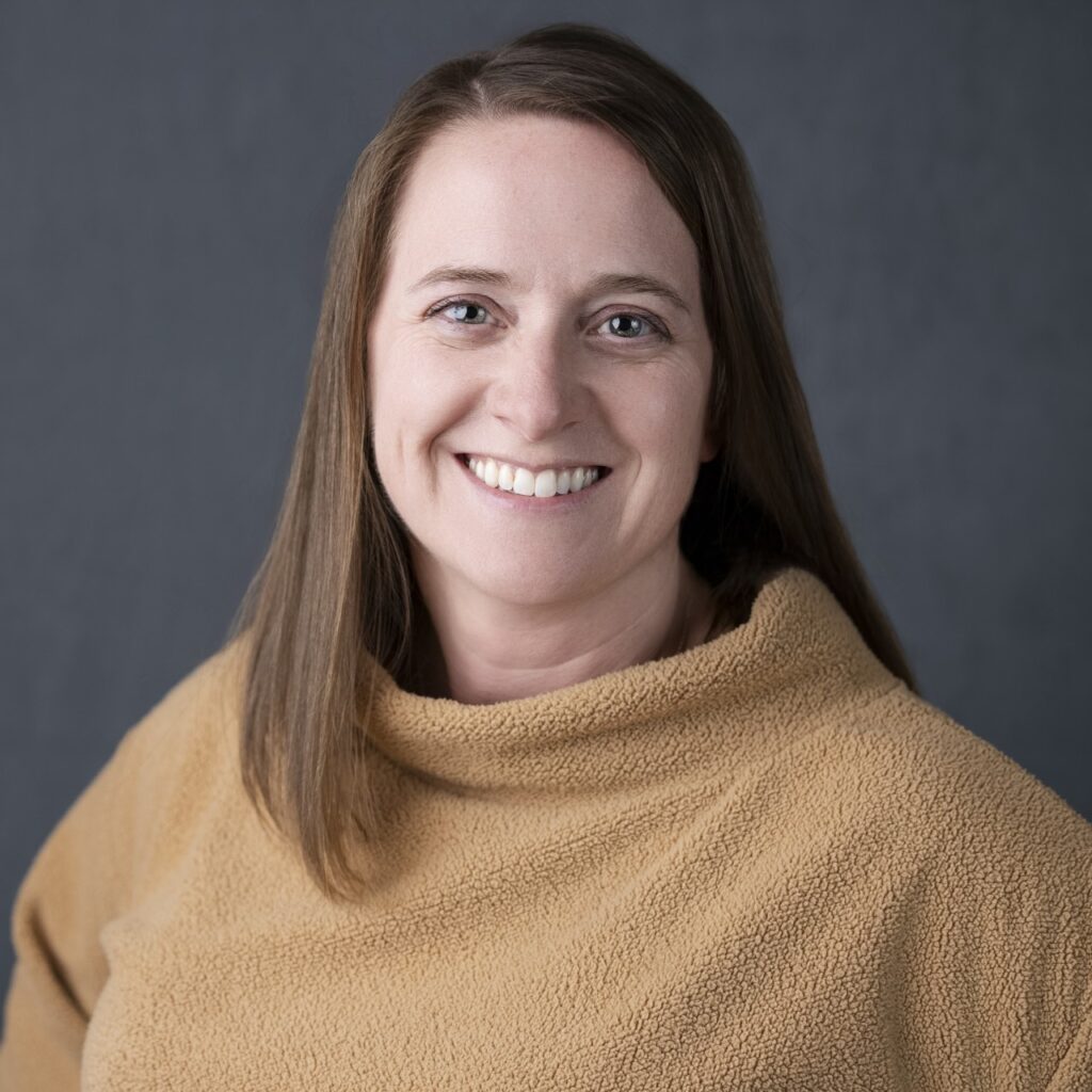 A smiling woman with long brown hair wearing a fuzzy beige sweater.