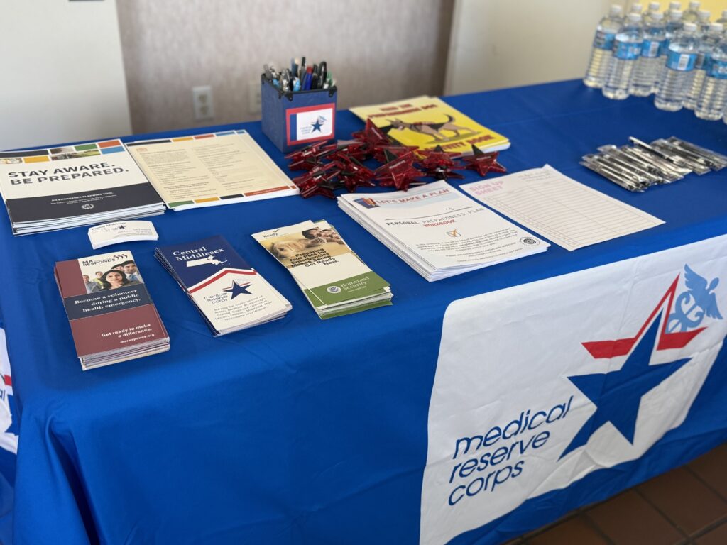 A table with a blue Medical Reserve Corps tablecloth. The table has pamphlets, pens, and other items.